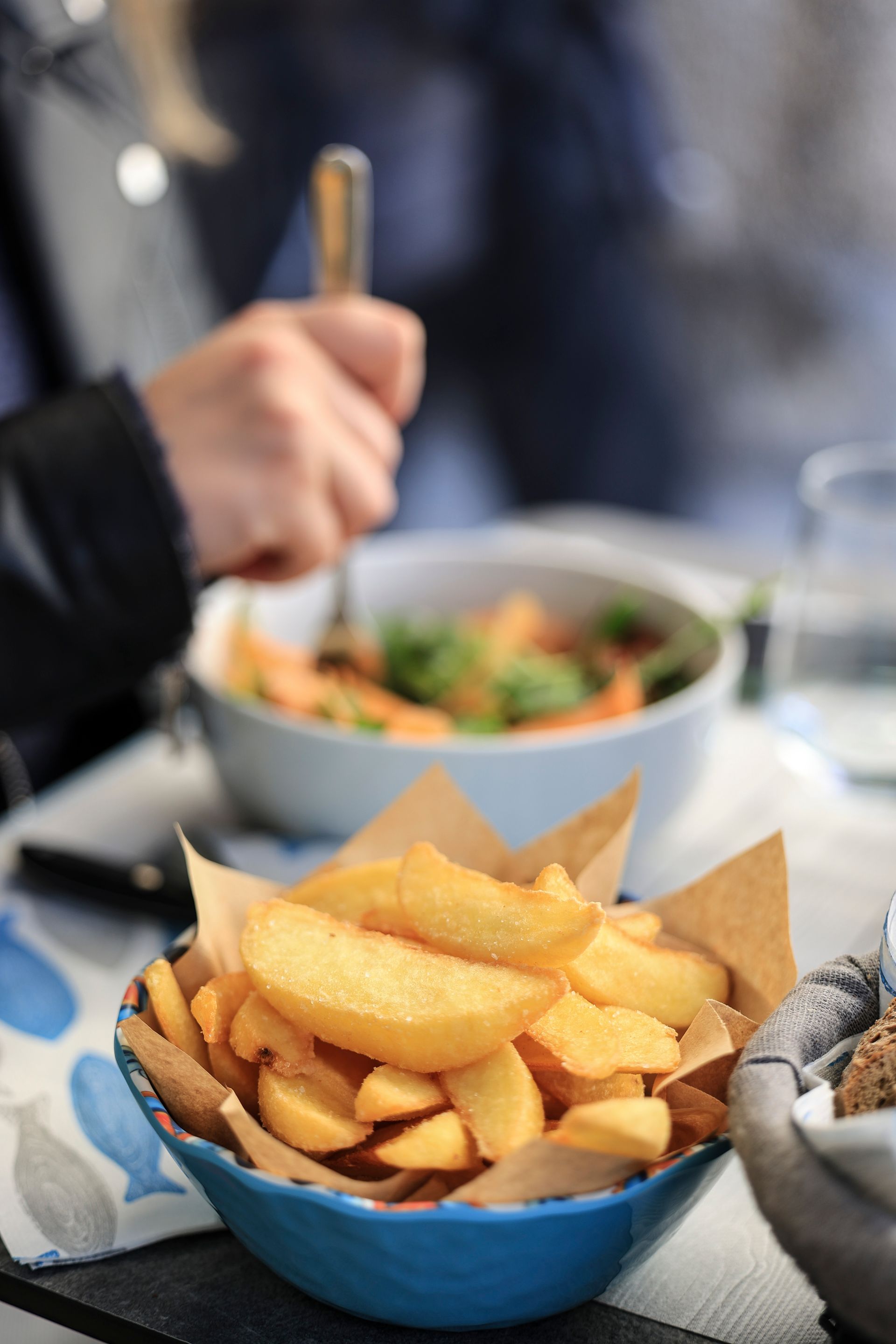 Una ciotola blu di tortilla chips su un tavolo, con una persona che mangia zuppa sullo sfondo sfocato.