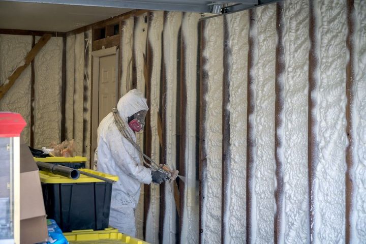 Worker in protective suit installing spray foam insulation inside a wall cavity