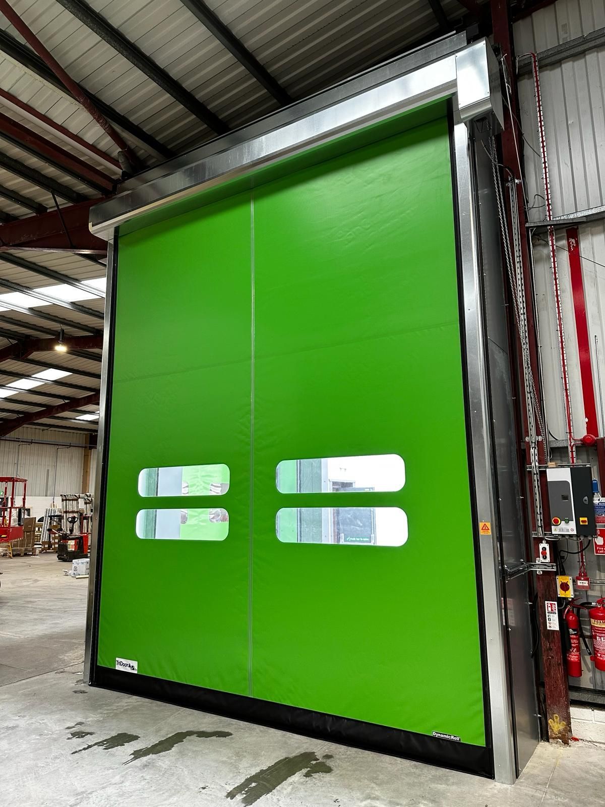 Bright green high-speed industrial rolling door with horizontal viewing windows installed in a warehouse.