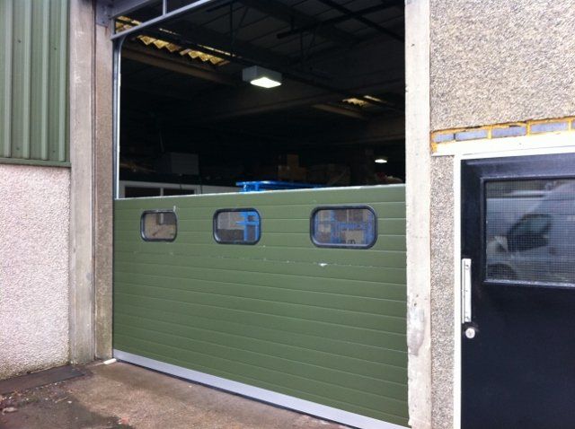 A green garage door with a black door behind it