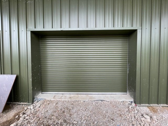 A green garage door is sitting on the side of a building.