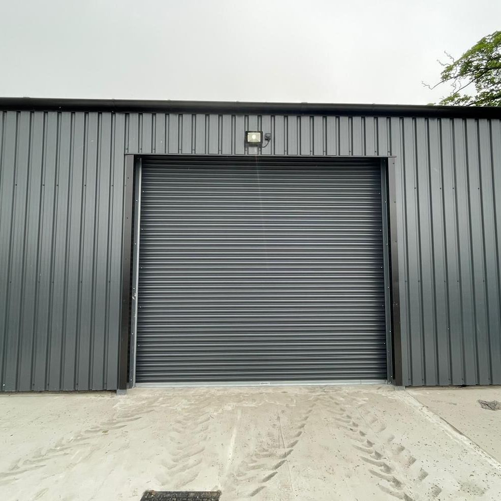 A grey industrial storage building with a central metal roller shutter door and a light fixture mounted above.