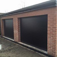 There are two black garage doors on a brick building.