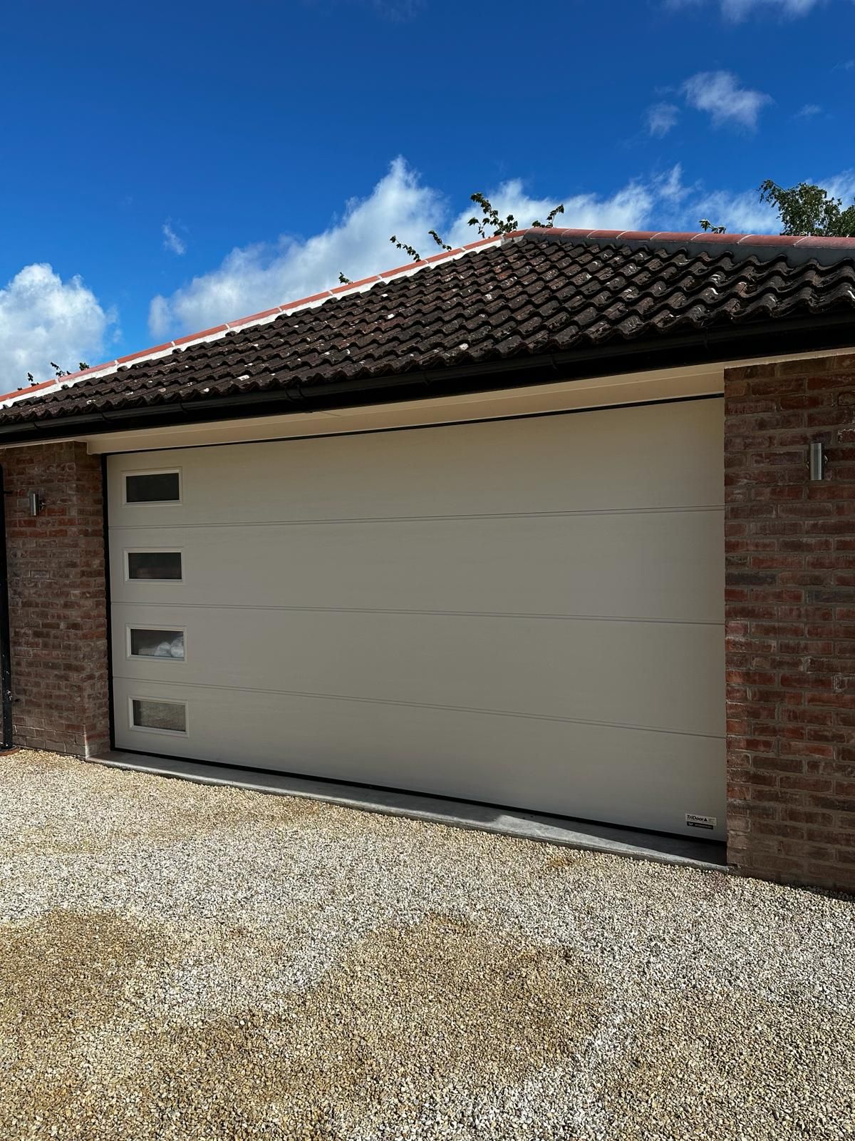 A wide, cream-colored sectional garage door with four vertical rectangular windows, set in a brick building.