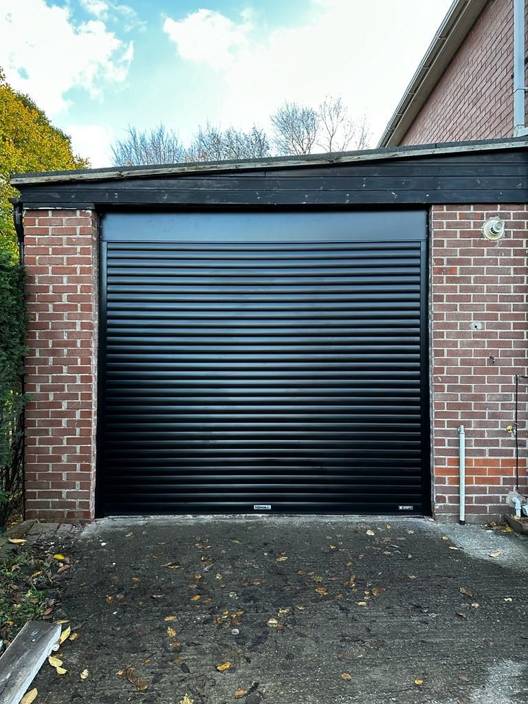A closed, black roll-up garage door set into a red brick building with a dark trim fascia.