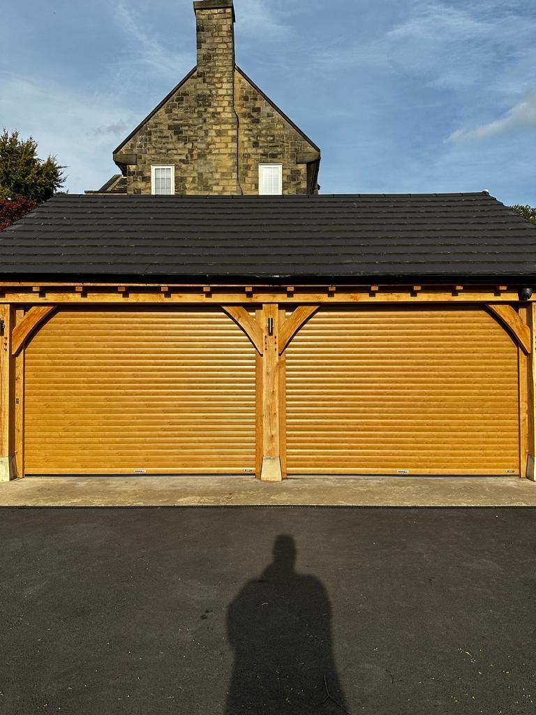 A double-bay timber-framed garage with closed horizontal slatted doors under a dark tiled roof, seen in daylight.