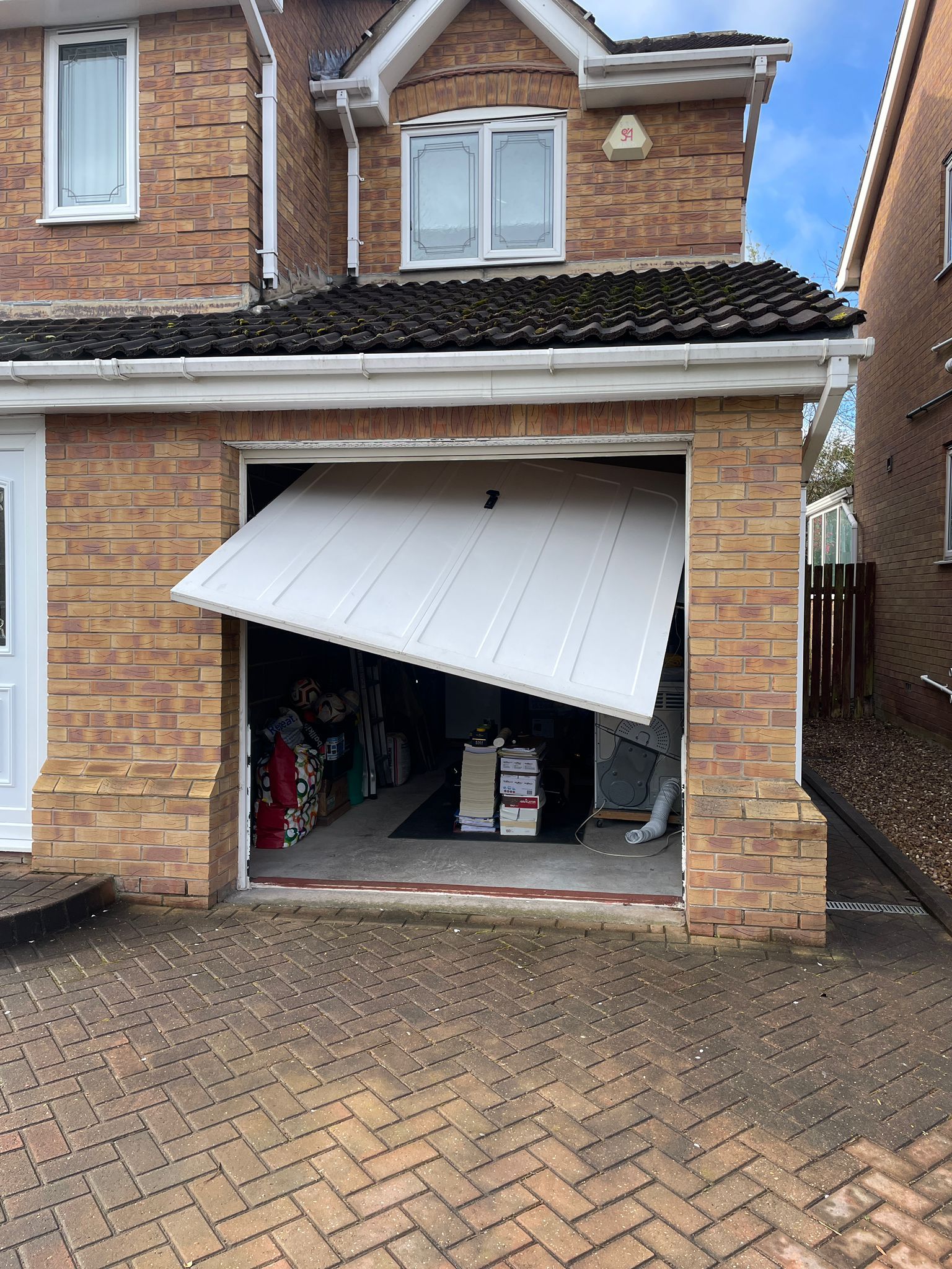 A white residential garage door hanging off its track and tilted at an angle on the front of a brick house.