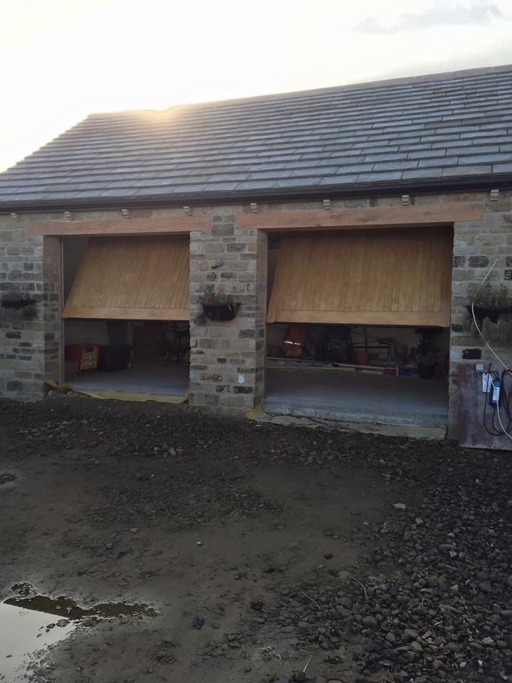A stone garage building with two open timber-clad canopy garage doors, set against a muddy yard at sunset.