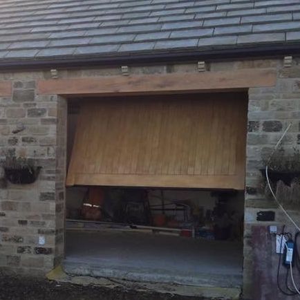 A partially opened wooden garage door on a stone building with a slate roof.