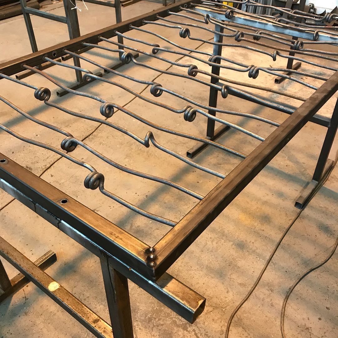 A rectangular metal frame contains parallel rebar rods with decorative spiral twists, appearing to be a custom furniture.