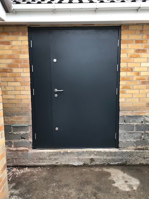 A dark gray, rectangular metal door with a silver handle set in a brick wall above an unfinished concrete step.