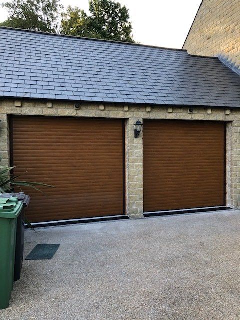 Two brown horizontal-slatted garage doors set in a stone building with a dark slate roof.