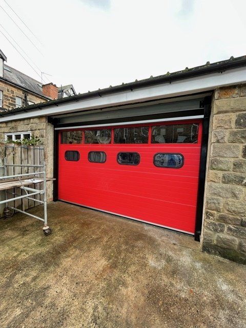 A bright red garage door with rectangular windows, set into a stone building.