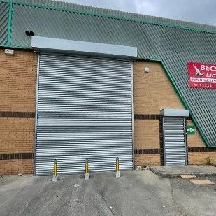 A large industrial building featuring a wide gray metal rolling shutter door next to a smaller matching pedestrian door.