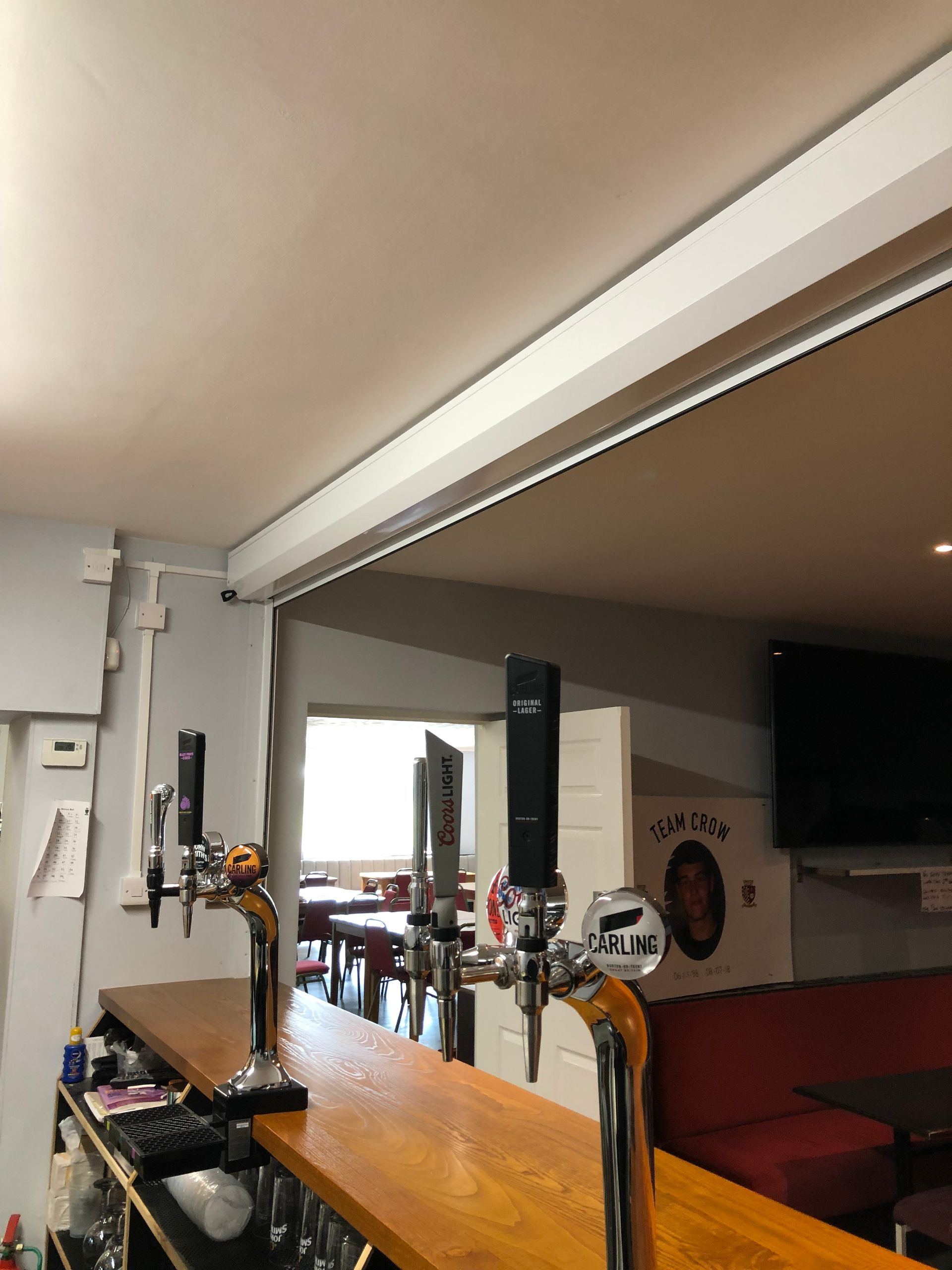 A close-up of two beer taps on a wooden bar inside a pub, with seating and a television visible in the background.