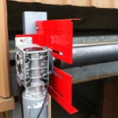 A red machine is sitting on top of a metal pipe.