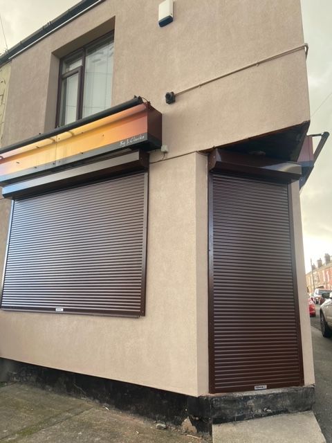 A beige corner storefront with brown security shutters closed over the windows and entrance door.