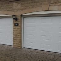 Two white garage doors on a light stone house with a lamp and address sign between them.
