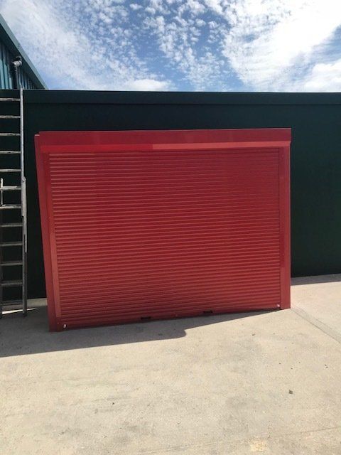 A red garage door is sitting in front of a green building