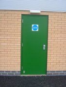 A green door with a blue sign on it is on a brick wall.