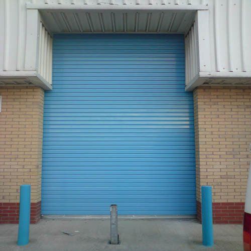 A blue garage door is sitting in front of a brick building.