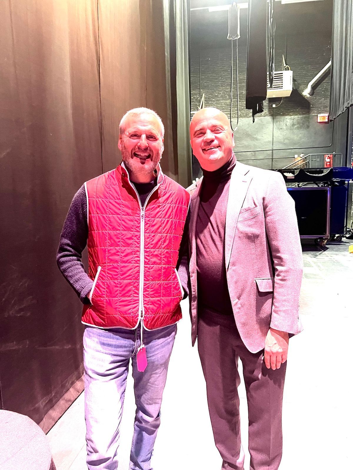 Two men standing backstage beneath stage lighting