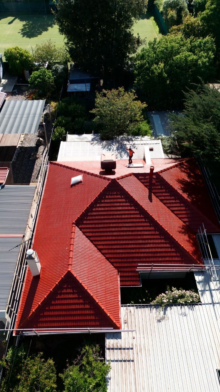 Aerial view of a red-roofed house surrounded by trees and neighboring rooftops.