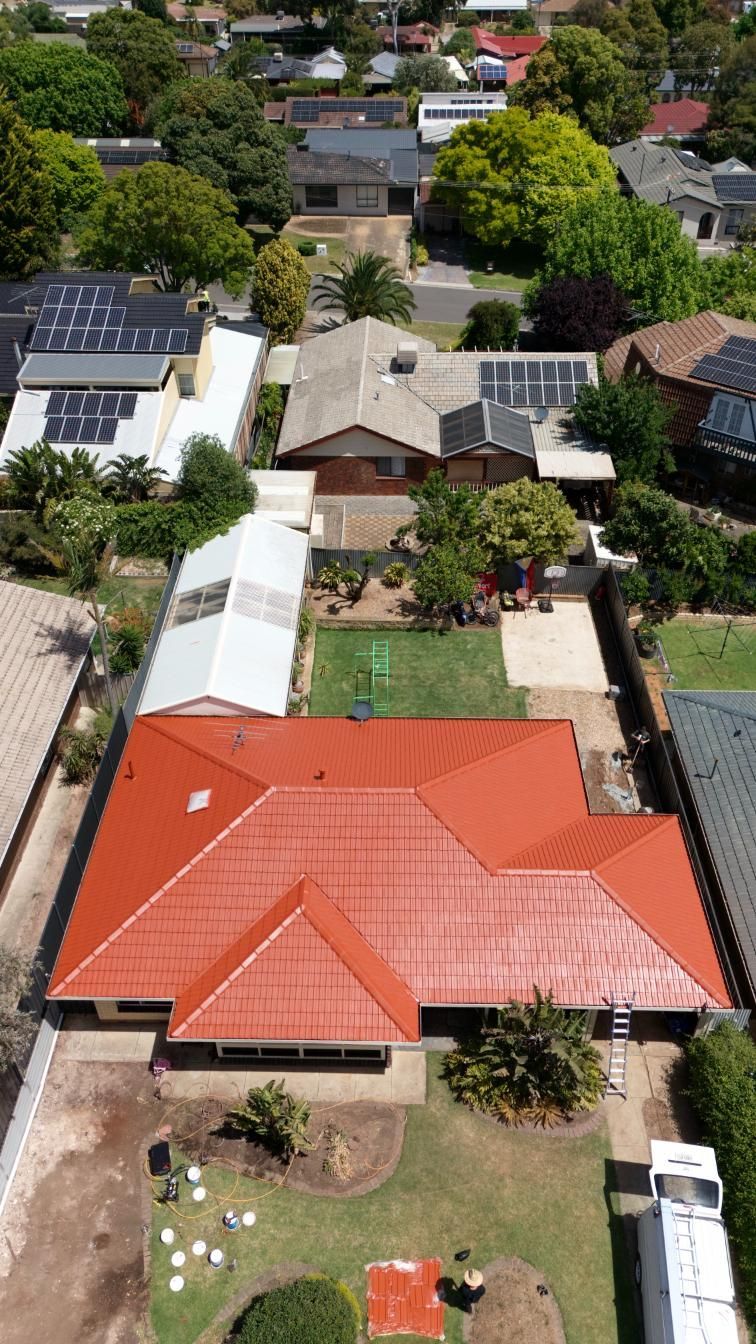 Aerial view of a neighborhood with red-roofed houses, solar panels, trees, and gardens.