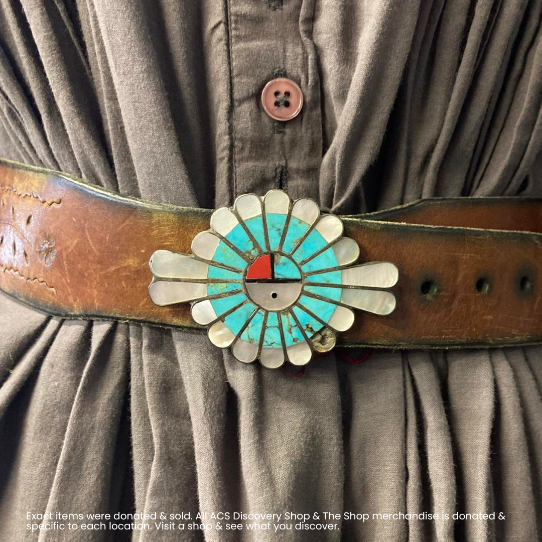 Close-up of a brown leather belt with a turquoise and white floral buckle over a pleated gray shirt