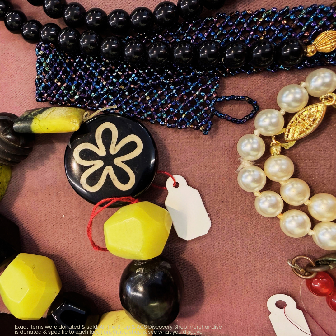 Assorted colorful beads, pearl strands, and small charms scattered on a pink surface.