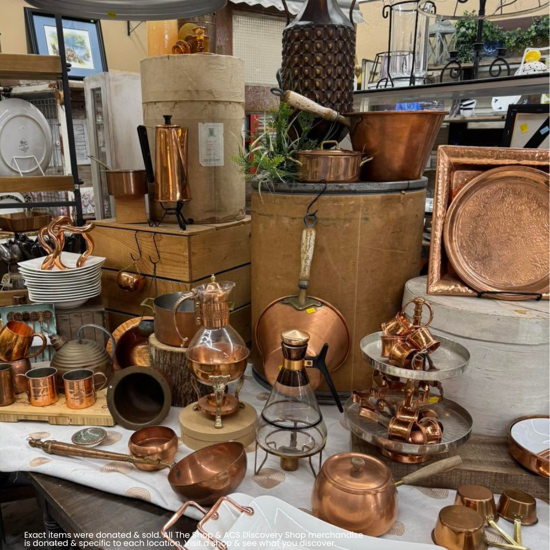 Antique copperware and brass cookware displayed on tables and shelves in a rustic market stall.