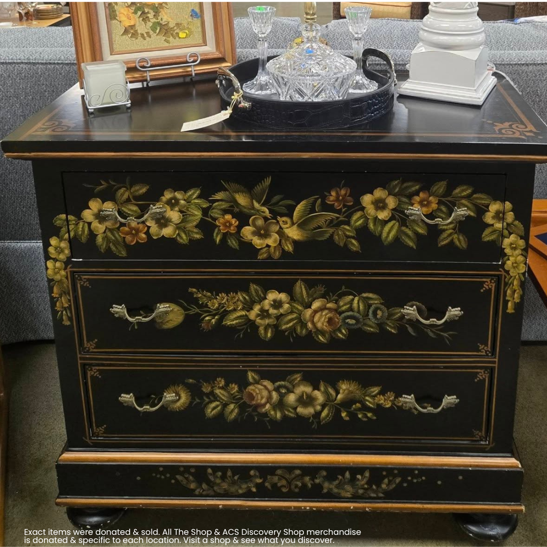 Black dresser with floral painted drawers, brass handles, and decorative glass items on top