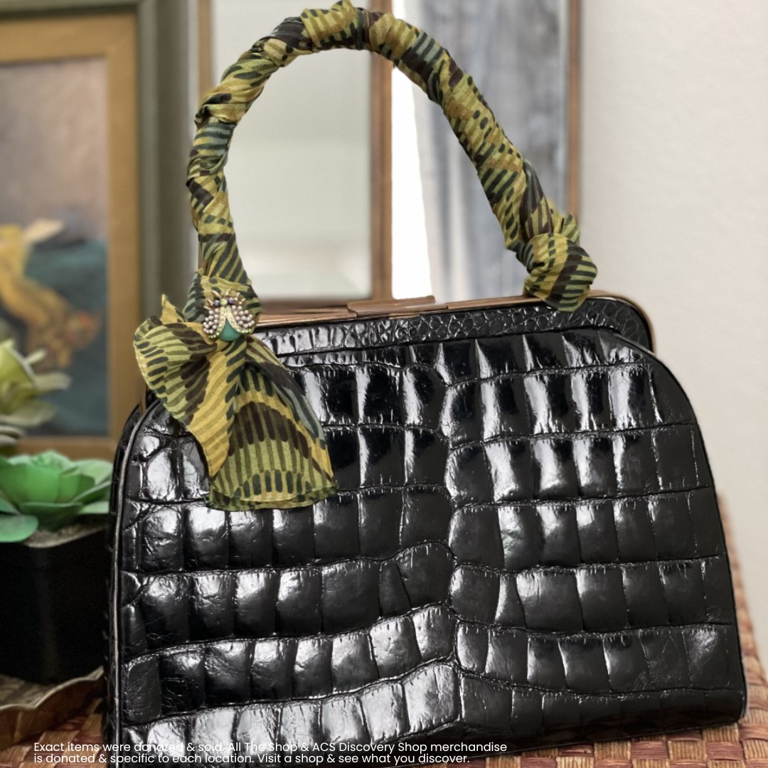 Black quilted handbag with a green patterned handle and scarf detail on a table