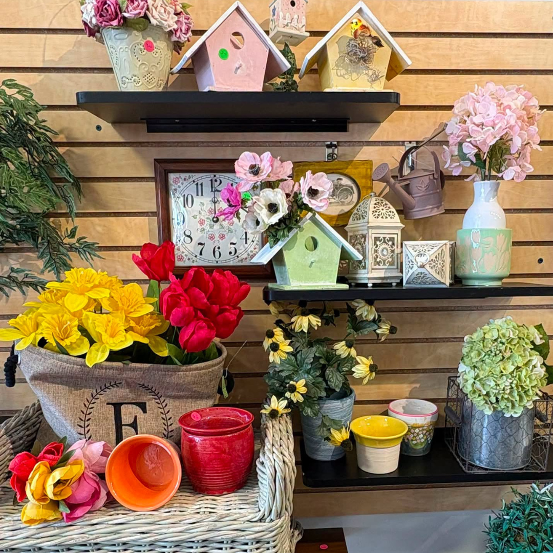 Rustic flower shop display with colorful potted blooms, birdhouses, candles, and decorative shelves