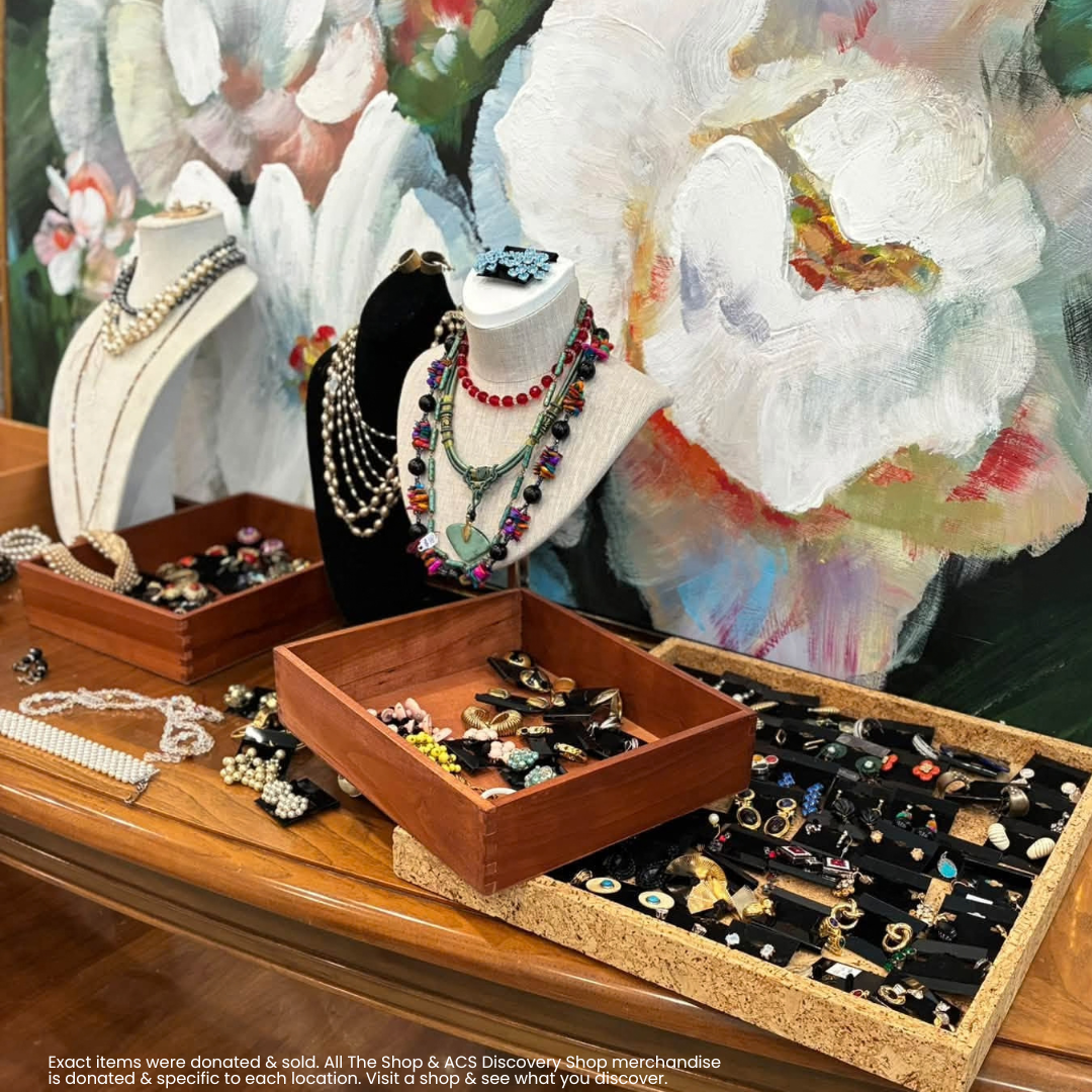 Jewelry display with necklaces and rings on wooden trays against a painted floral backdrop