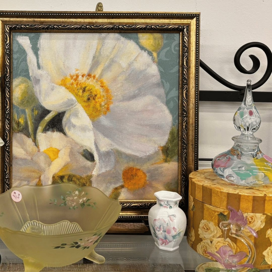 Still life of white flower artwork with decorative glass bowls, vase, and gold box on a shelf