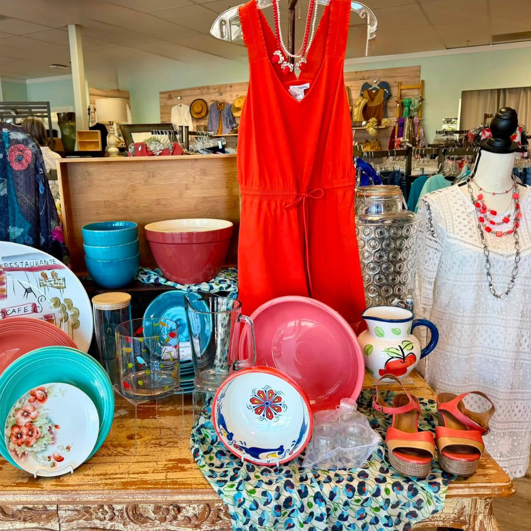 Bright red dress displayed among colorful vintage dishes and jewelry in a shop window.