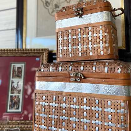 Two woven wicker boxes with silver bands stacked on a table in a room