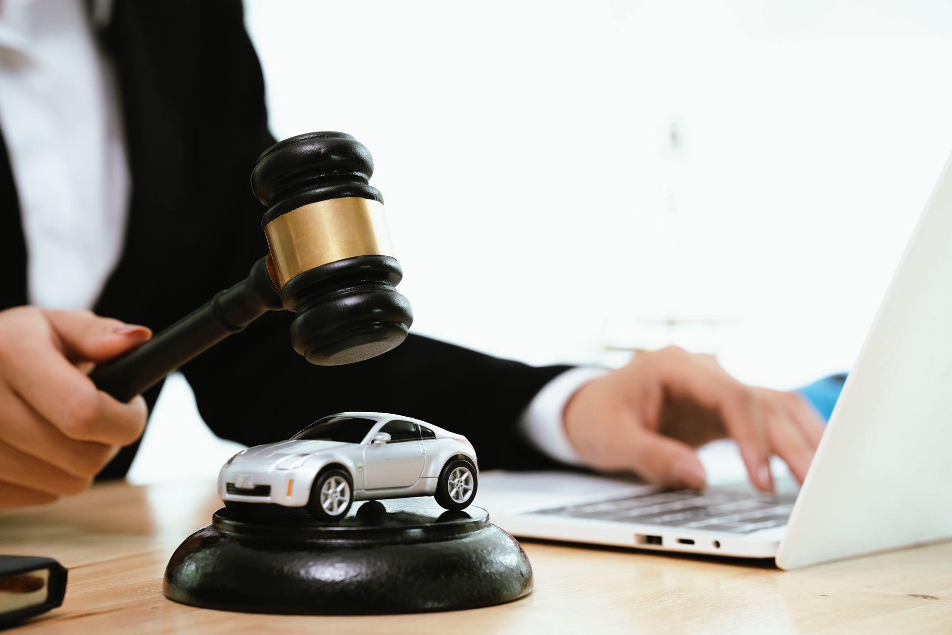 A lawyer in a suit uses a gavel near a toy car on a base. A lawyer in a suit uses a gavel near a toy car on a base.