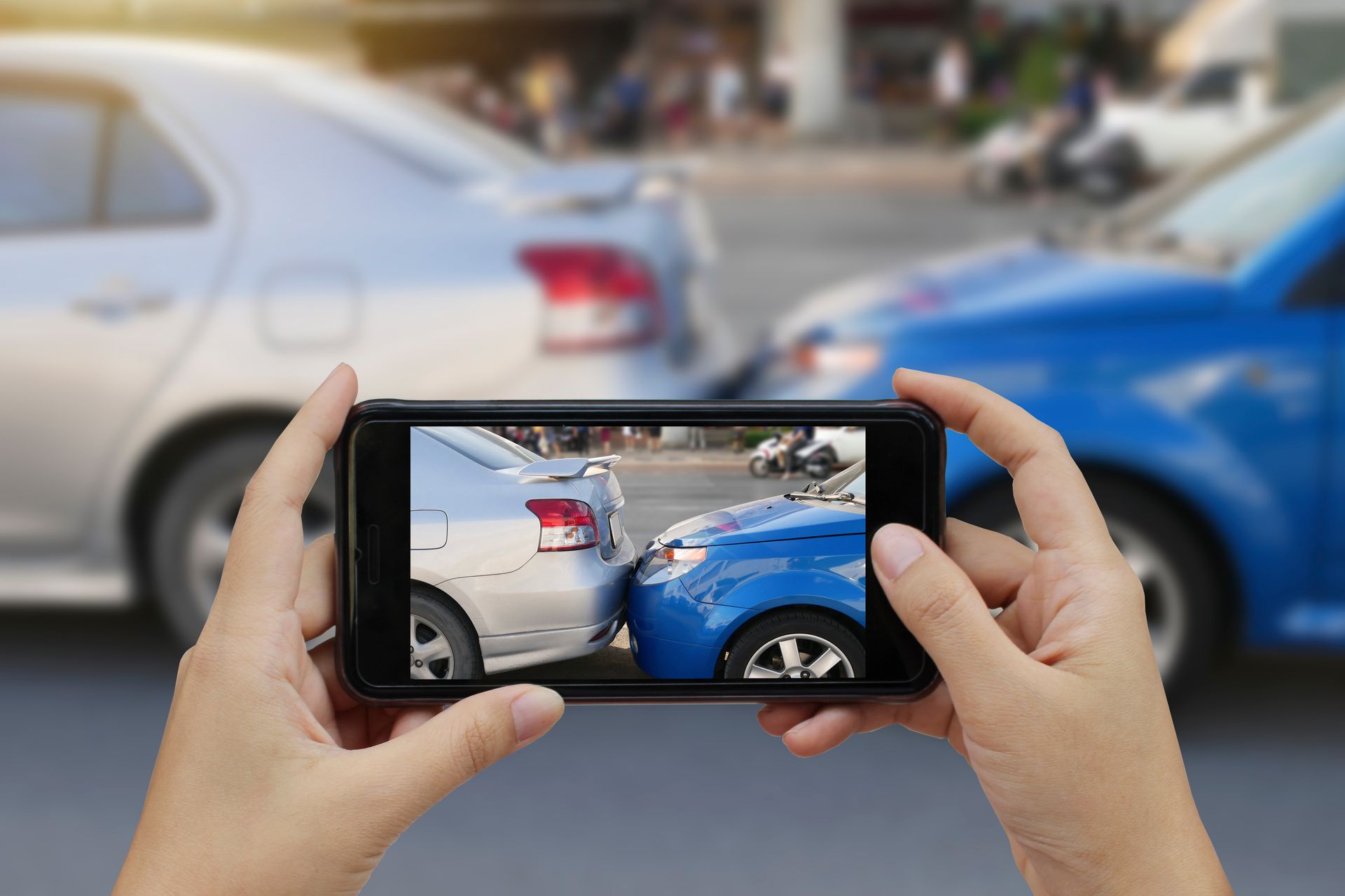 A person's hand is holding a smartphone and taking a photo of a car accident. A person's hand is holding a smartphone and taking a photo of a car accident.