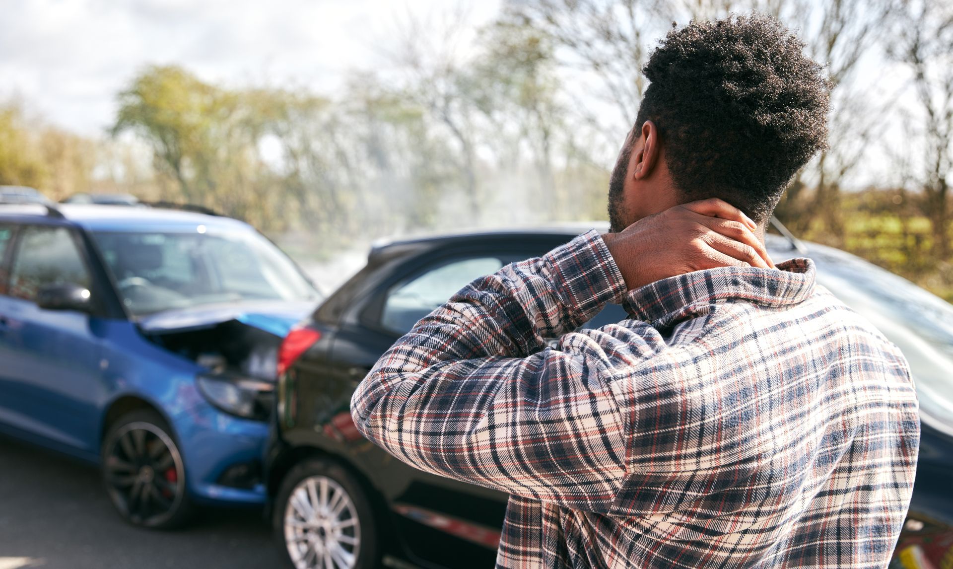 Injured driver holding his neck beside damaged vehicles after a car accident
