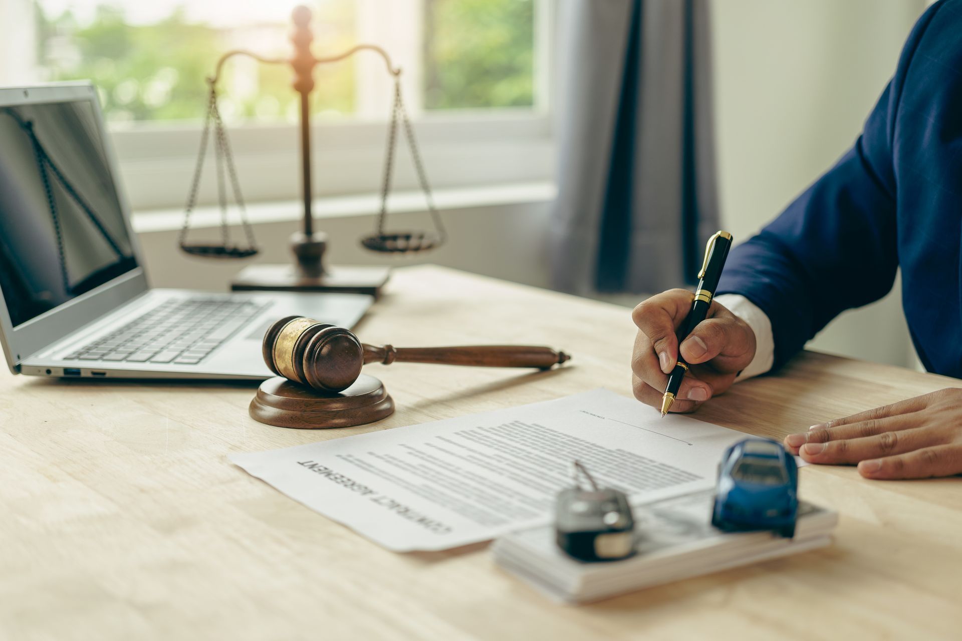 An auto accident attorney is working in his office, with a gavel and a miniature car on his desk.