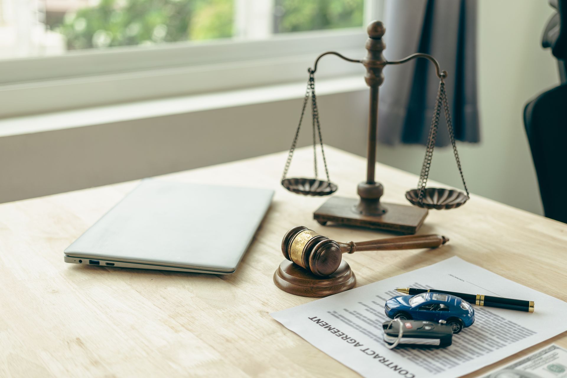 Legal desk with scales of justice, gavel, and car accident documents with a toy car and keys.