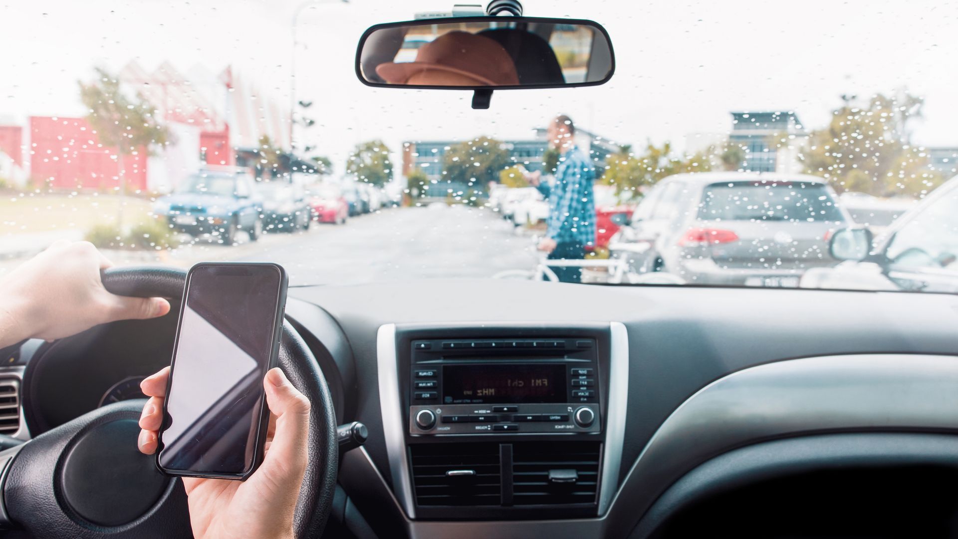 Person in car texting while approaching pedestrian in parking lot.