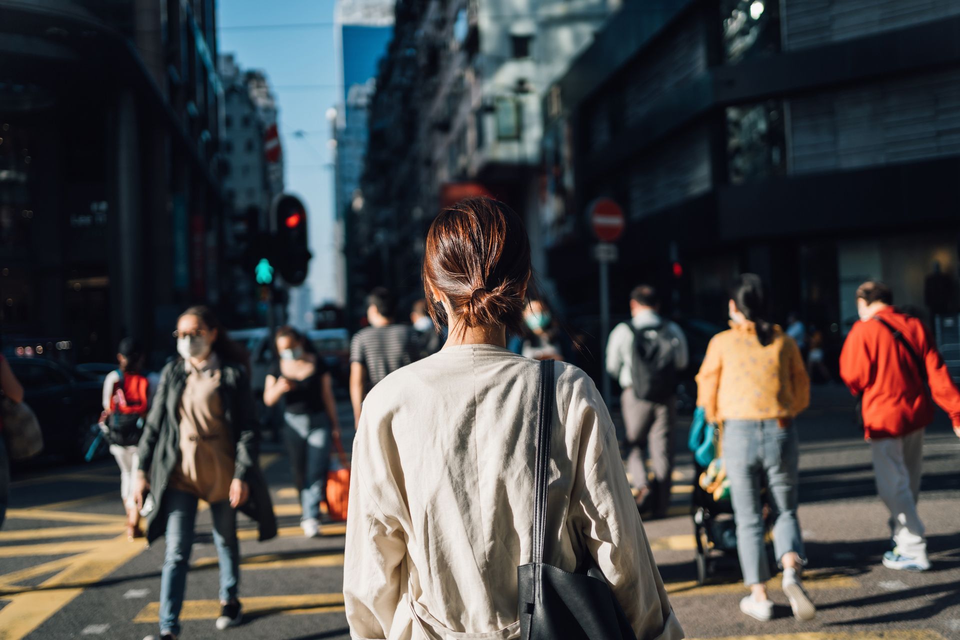 Woman walking in a city street, surrounded by pedestrians, buildings, and a traffic light.
