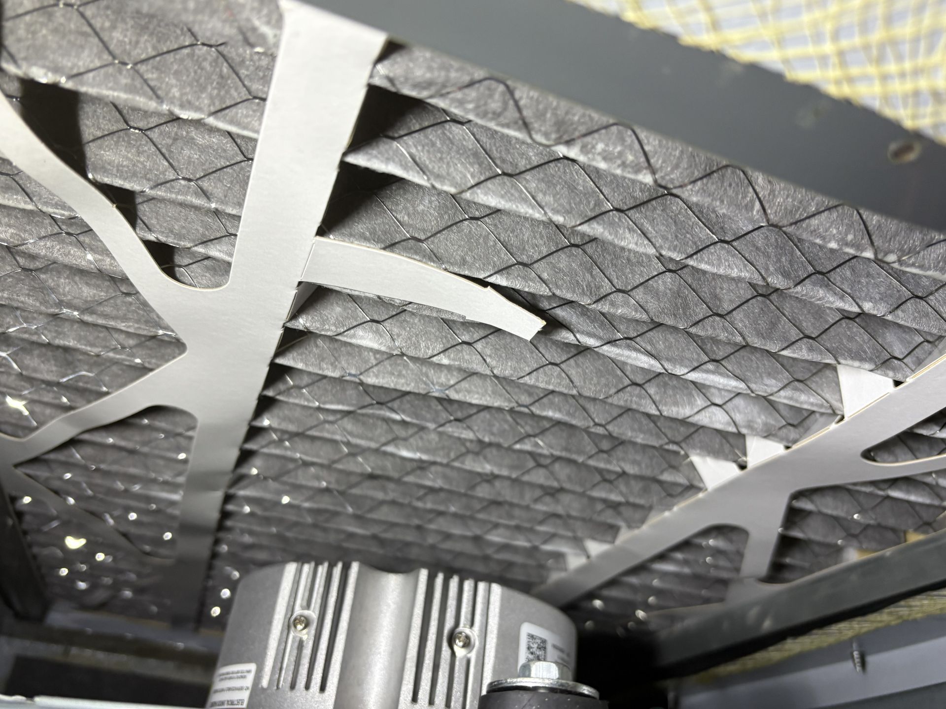 Close-up of a metal bed frame with gray mesh support and a silver cylindrical component underneath