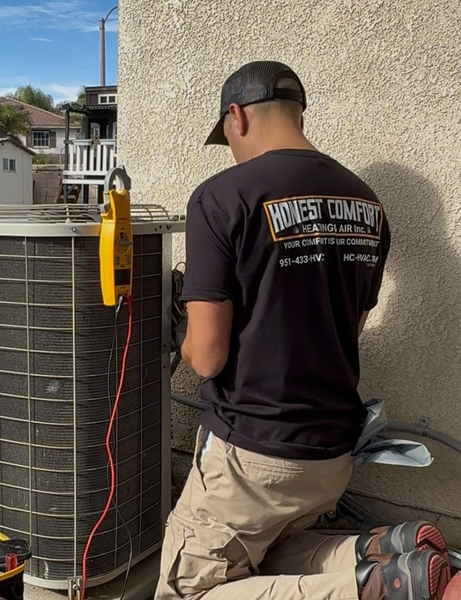 Technician kneeling beside rooftop HVAC unit, checking wiring against a stucco wall.