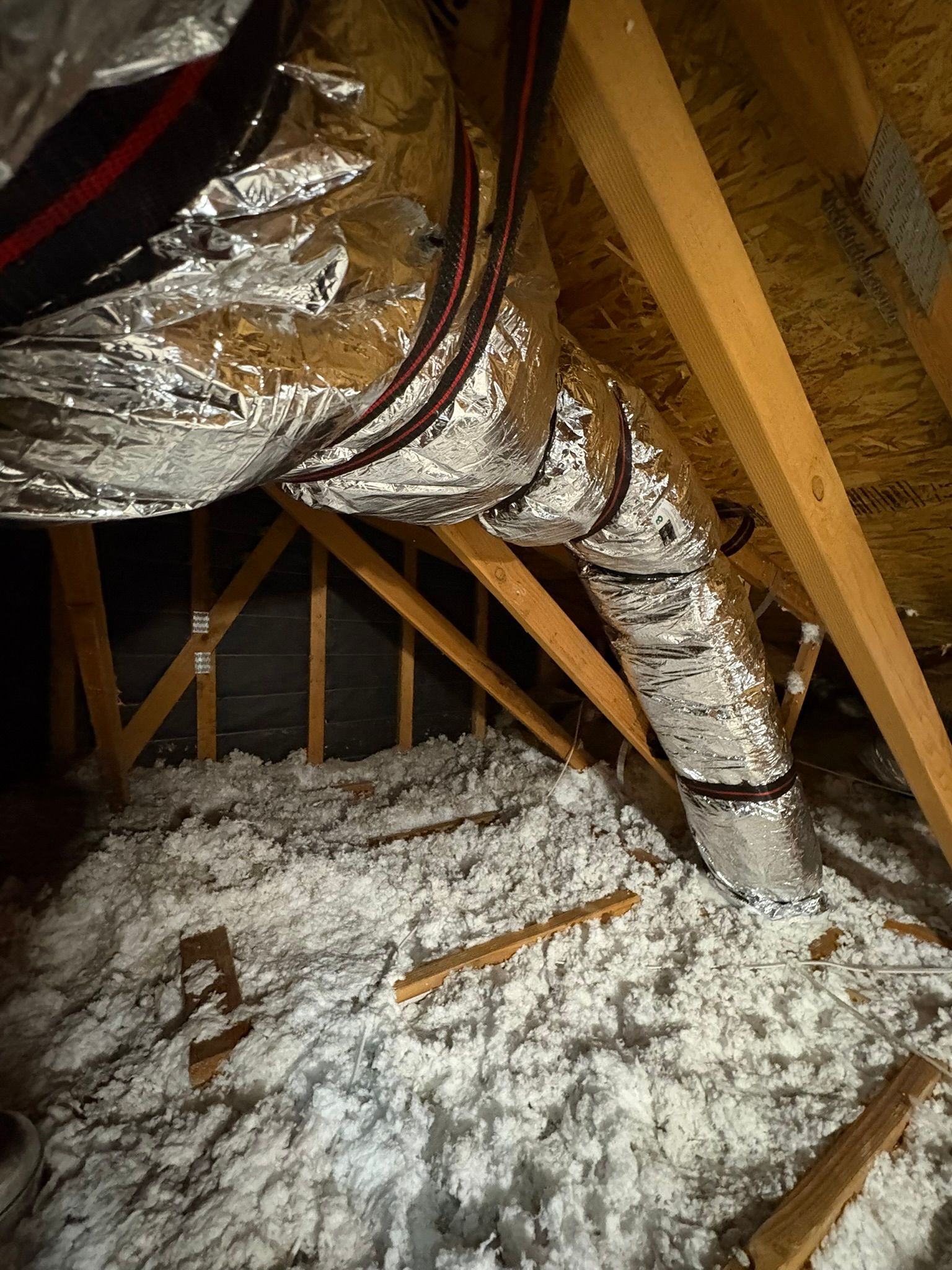Attic with exposed rafters and insulated ducts, with white insulation scattered on the floor