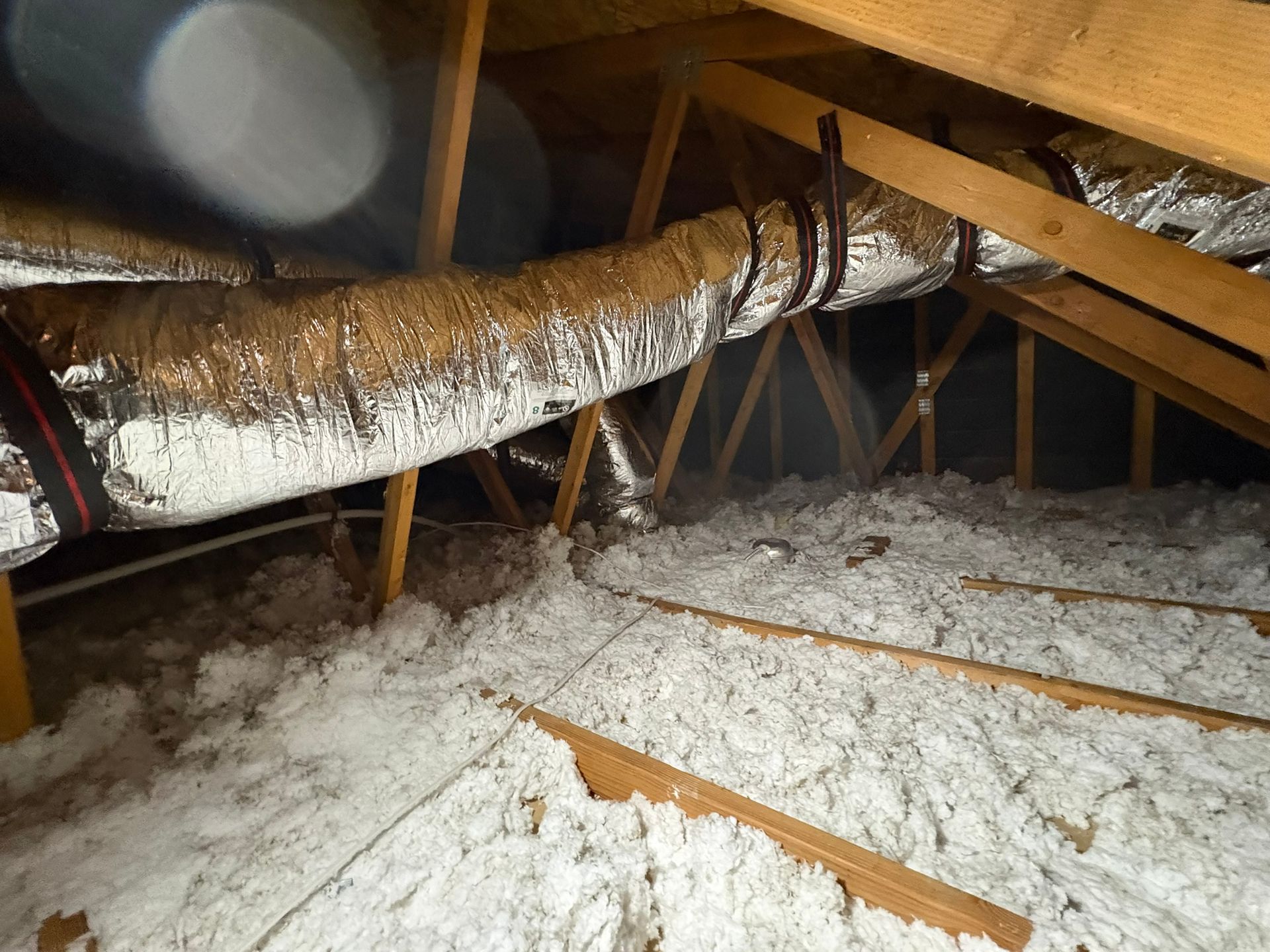 Attic with exposed ductwork, insulation, and wooden rafters under a sloped roof