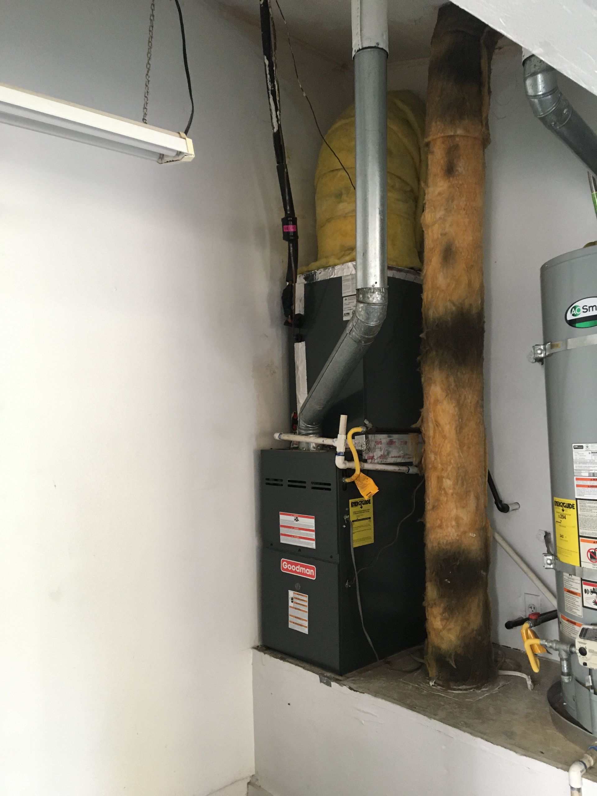 Basement furnace and water heater beside a concrete wall, with exposed pipes and ducting.